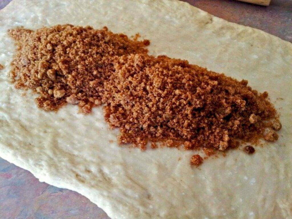 Brown sugar is spread in a thick line on a rectangular sheet of raw dough&mdash;just like preparing no yeast cinnamon rolls&mdash;which rests on a flat surface, ready to be rolled or folded.