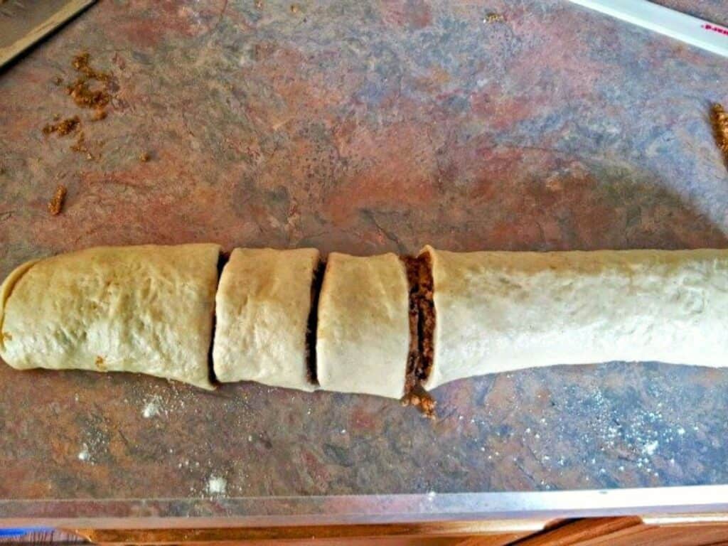 Rolled dough with a filling inside is partially sliced into sections on a countertop, resembling no yeast cinnamon rolls, and is ready for further preparation.