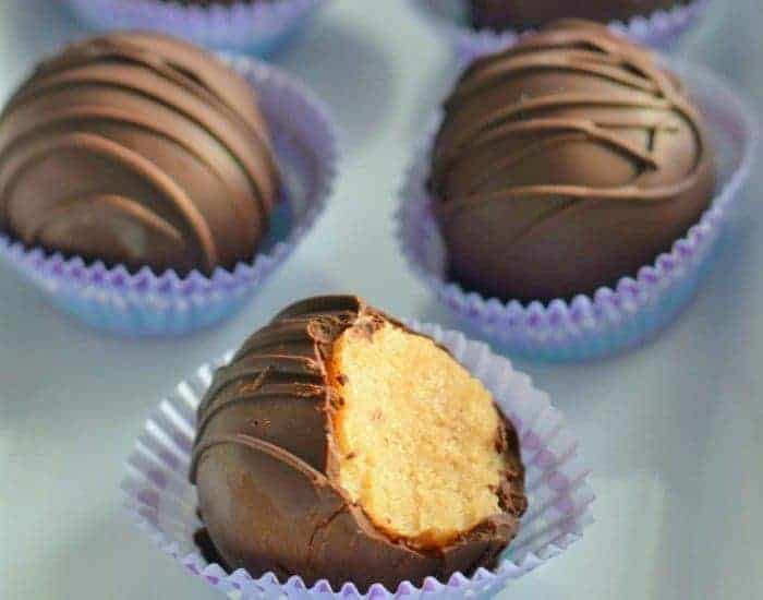 Image shows a bite taken from a brown sugar cookie dough truffle in a paper wrapper with two more behind it.