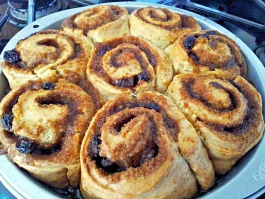 A round baking pan filled with freshly baked no yeast cinnamon rolls with raisins and a golden-brown crust.