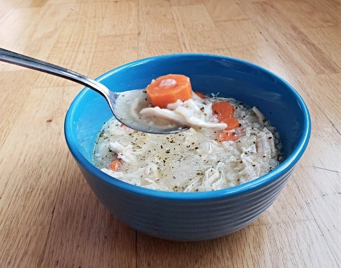 Image shows Chicken and rice soup on a spoon with the full blue bowl behind it.