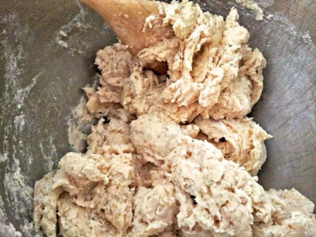 A metal bowl with thick no yeast cinnamon rolls dough being mixed with a wooden spoon.