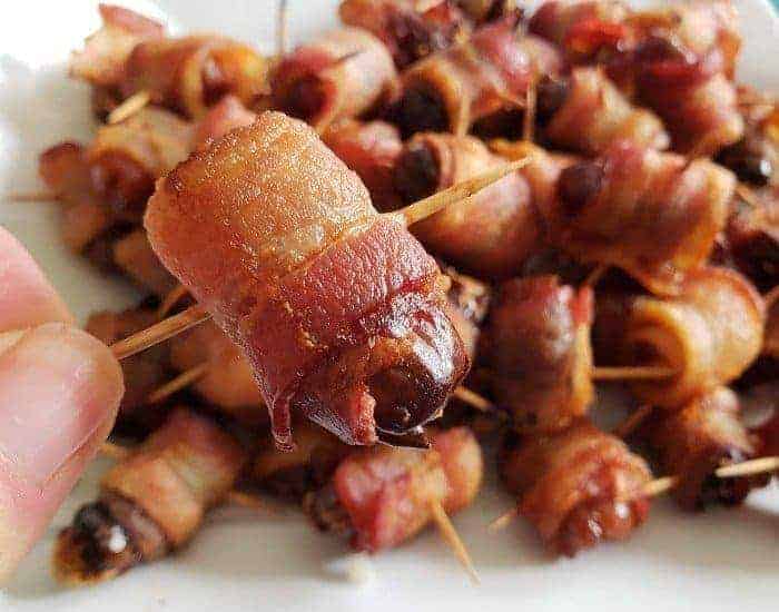 https://instagram.com/HonestAndTruly a hand holding a Homemade bacon wrapped date with more behind it.