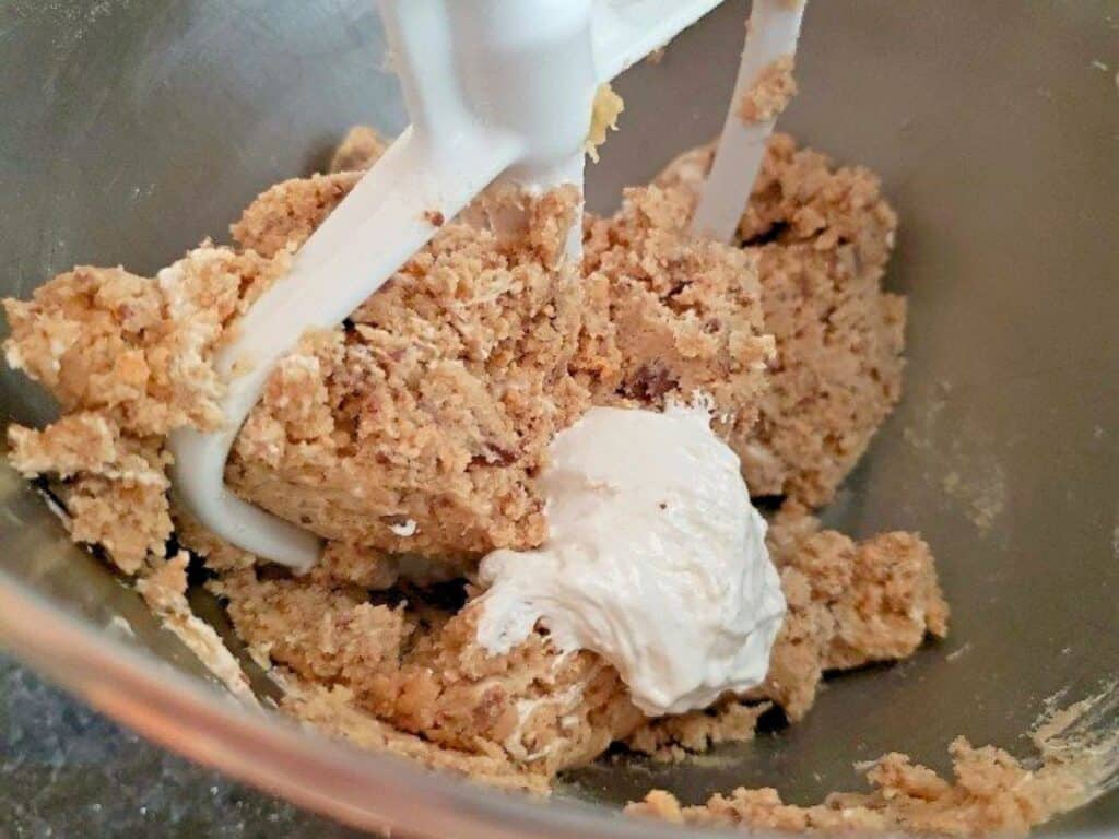 Close-up of edible s&rsquo;mores cookie dough being mixed in a stand mixer bowl, with a dollop of cream or batter sitting on top of the dough.