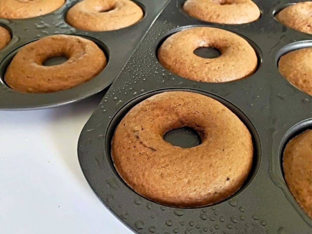 Close-up of freshly baked chocolate donuts in nonstick baking pans, with some condensation visible on the pans&rsquo; surface.
