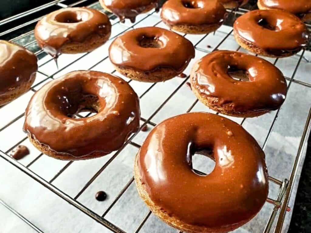 Chocolate-glazed donuts cooling on a wire rack with parchment paper underneath; some glaze drips are visible on the rack and paper.