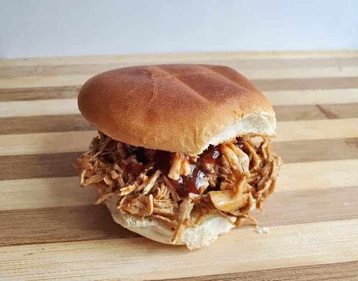 Image shows a BBQ shredded chicken sandwich on a wooden board.