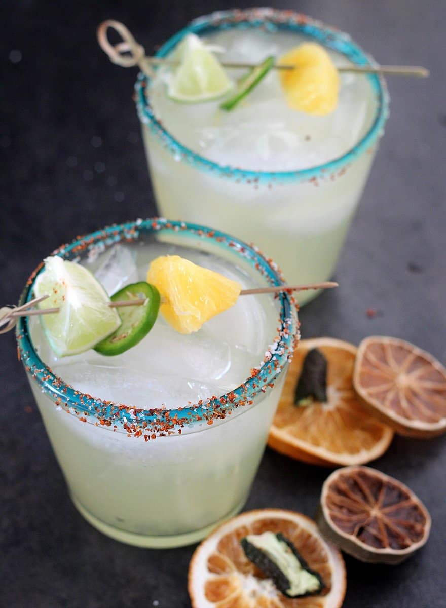 Two glasses of margaritas with salt and a lemon and lime garnish.