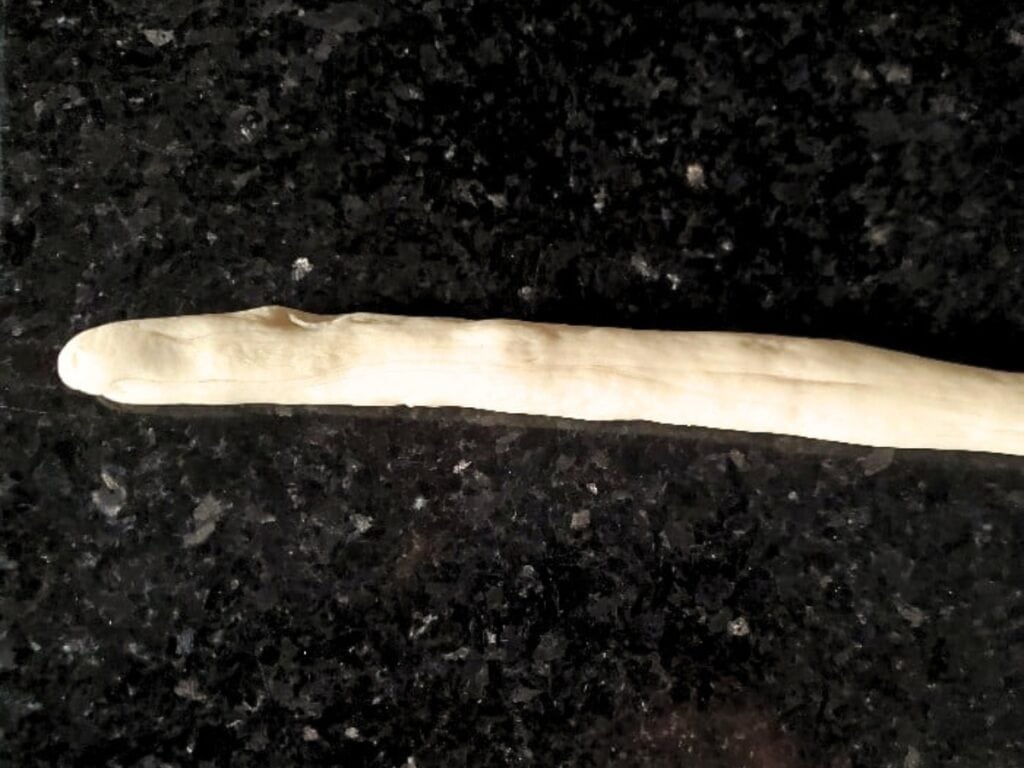 A long, thin strip of raw dough, soon to be transformed into delicious pretzel bites, is placed on a dark, speckled countertop.