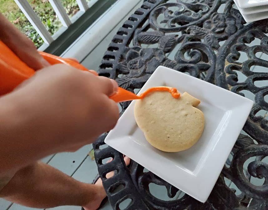 Outlining a pumpkin cookie in orange frosting