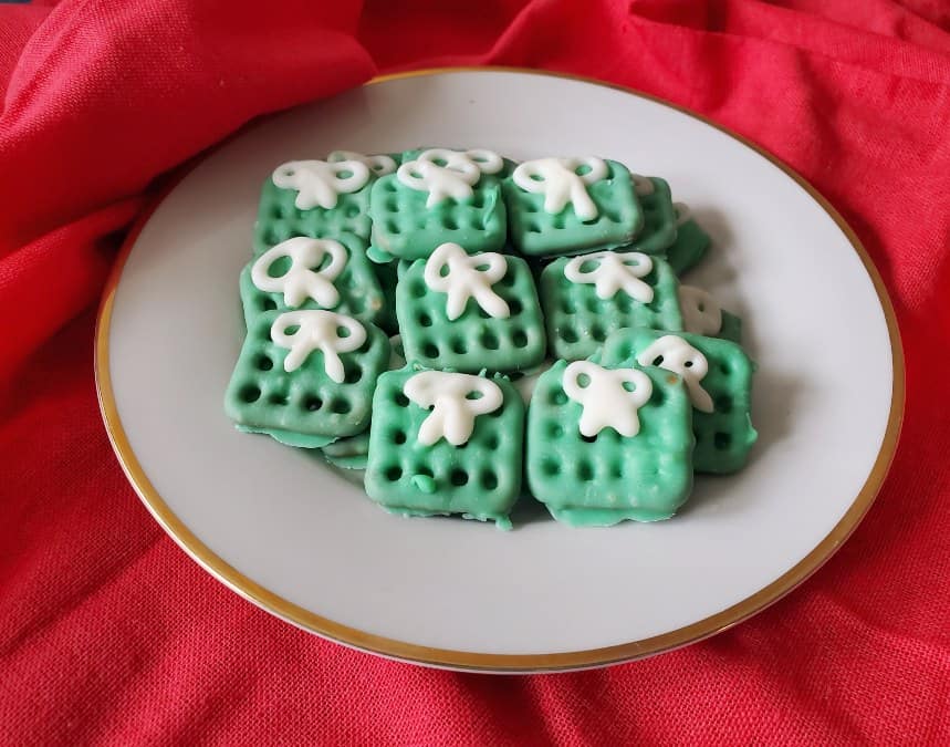 A plate of square-shaped green cookies with white icing decorations, arranged neatly, with a red cloth backdrop.