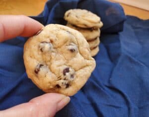 Holding a sourdough chocolate chip cookie in front a of a stack of more cookies.