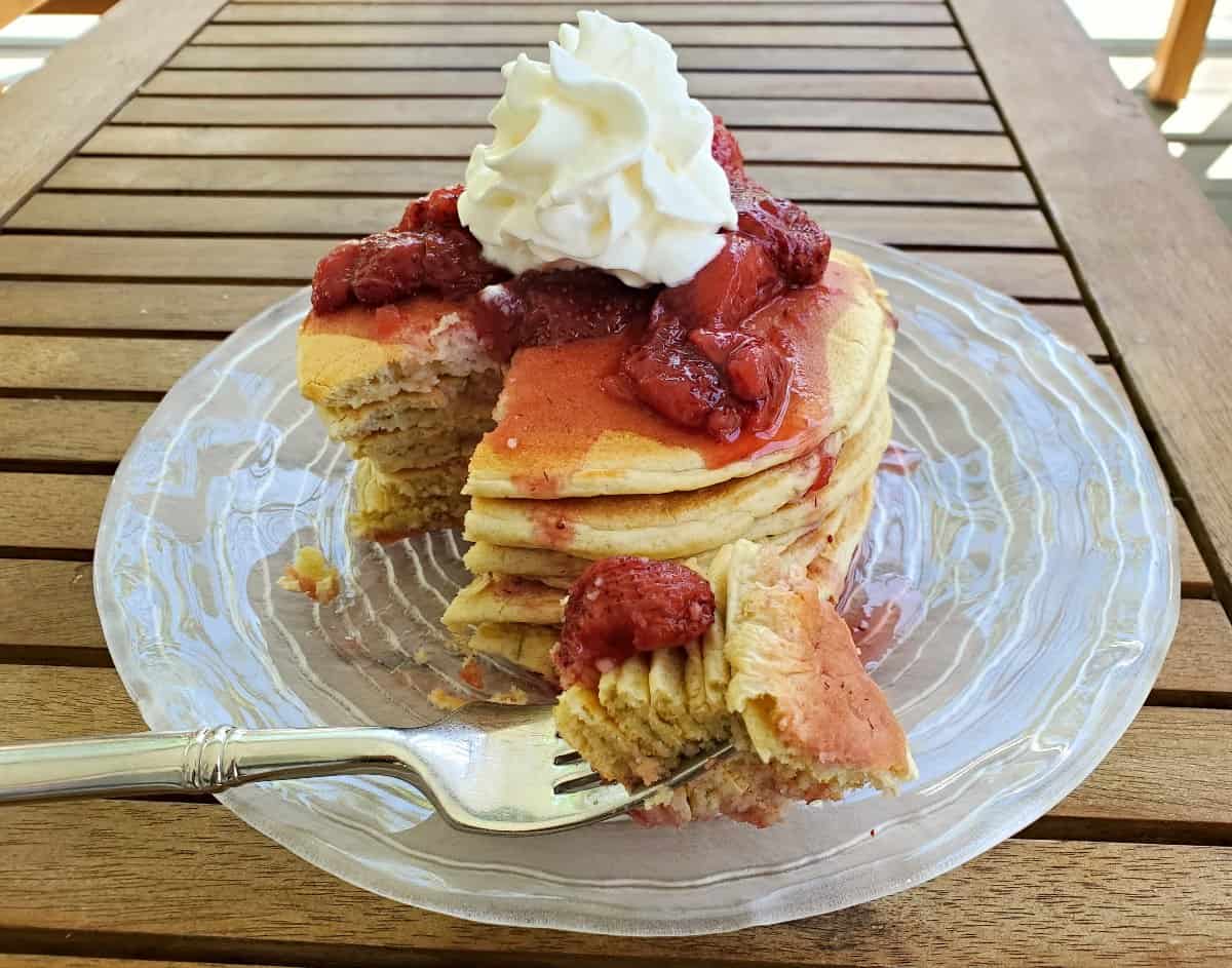Image shows an overhead shot of Sourdough Pancakes on a plate with strawberry syrup dousing them.