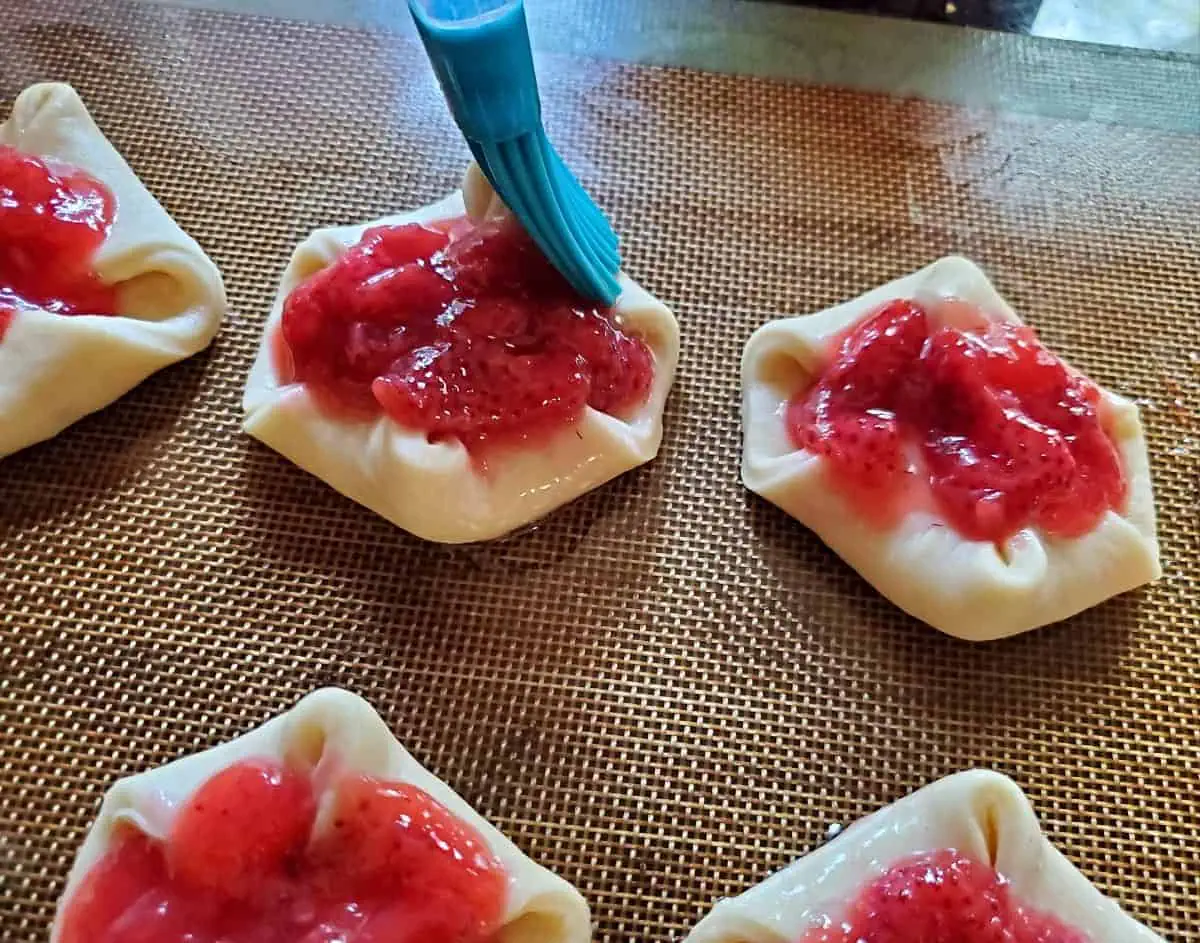 Brushing unbaked strawberry danishes with egg wash.