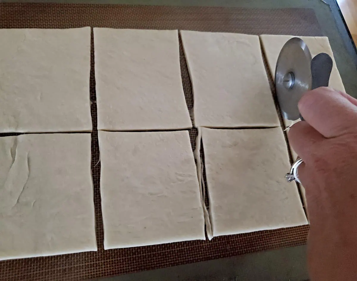 Crescent roll dough sliced into squares using a pizza wheel.