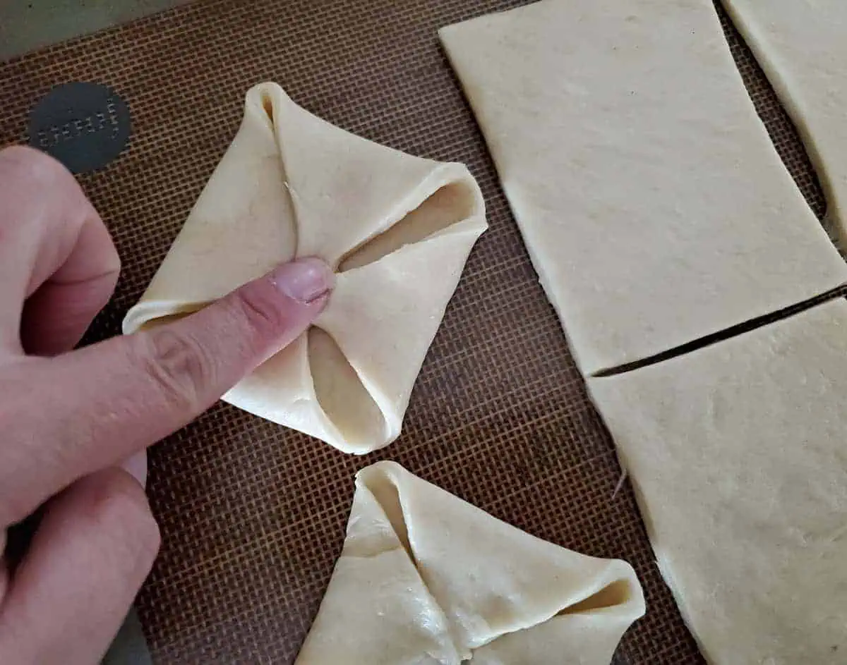 Finger pressing dough corners into center to form a pinwheel shape.