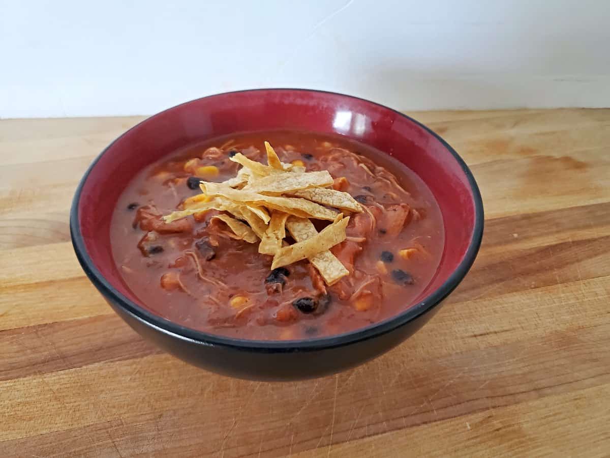 A bowl of chili with black beans, corn, and shredded chicken, topped with crispy tortilla strips.