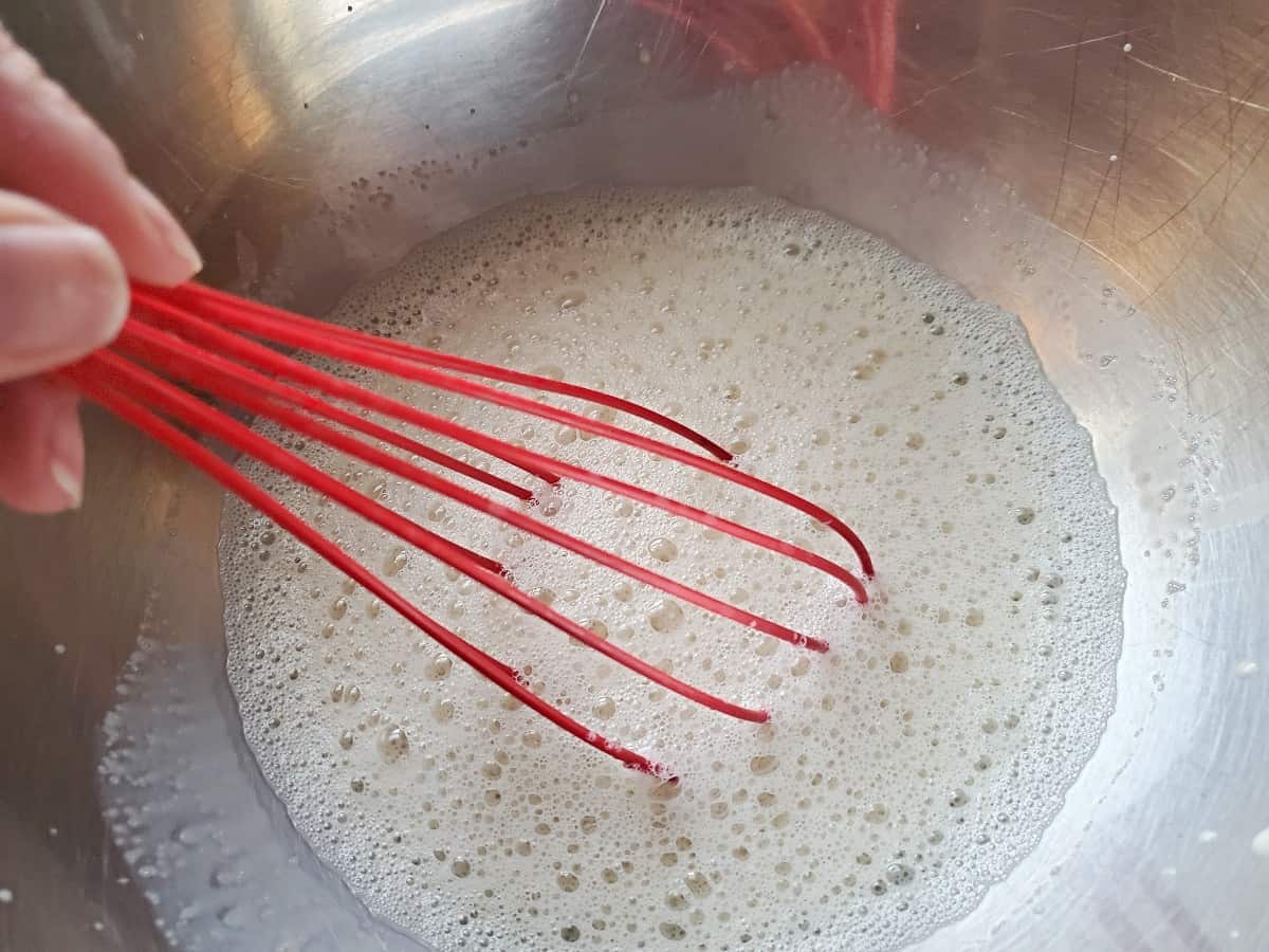 Whisked milk that is bubbly in a silver bowl.