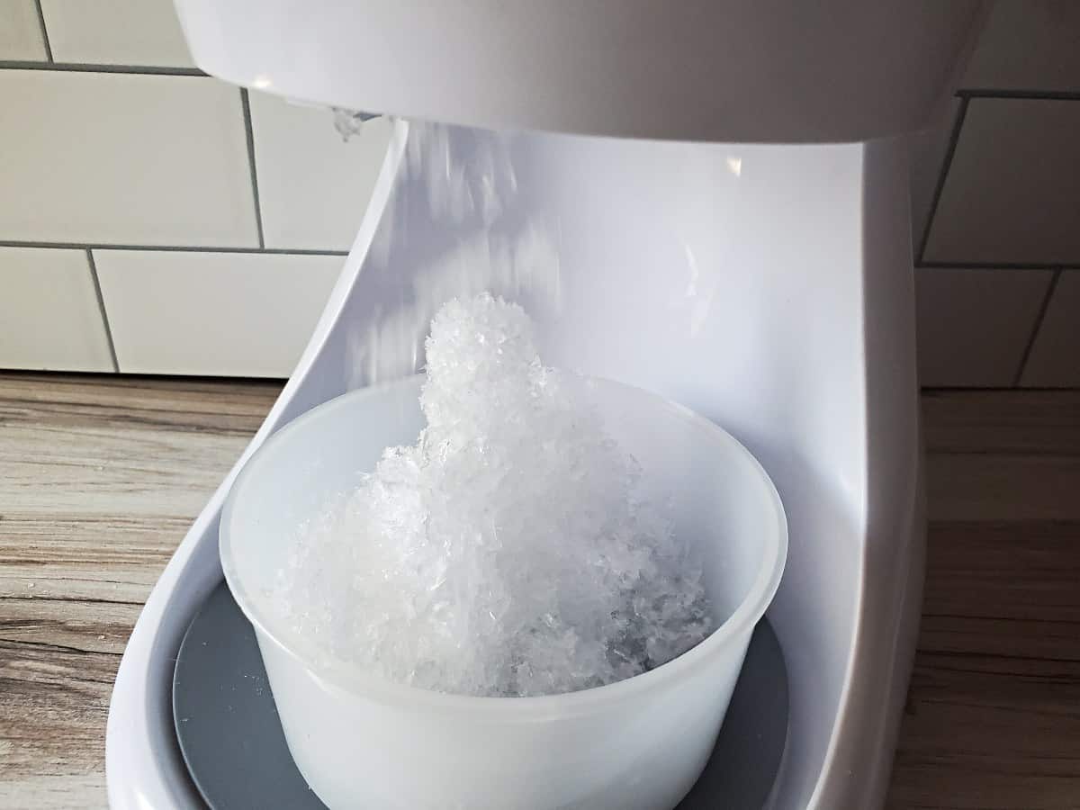 Ice being shaved by an electric maker into a small cup.