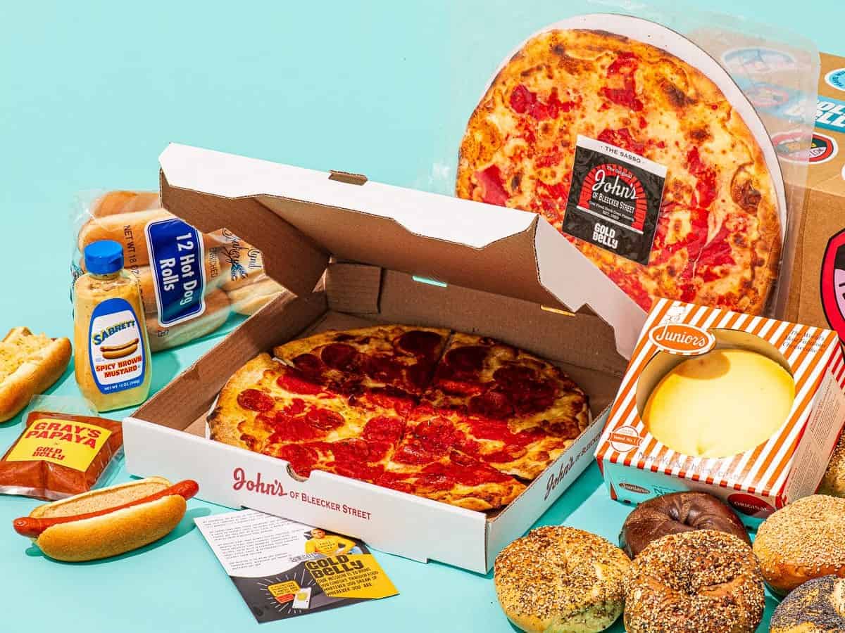 Image of traditional NYC foods from bagels to pizza to cheesecake arranged on a teal background.