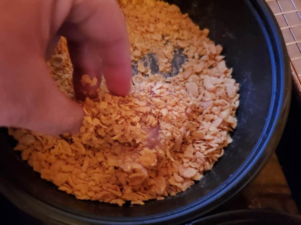 Coating chicken in crushed corn flakes.