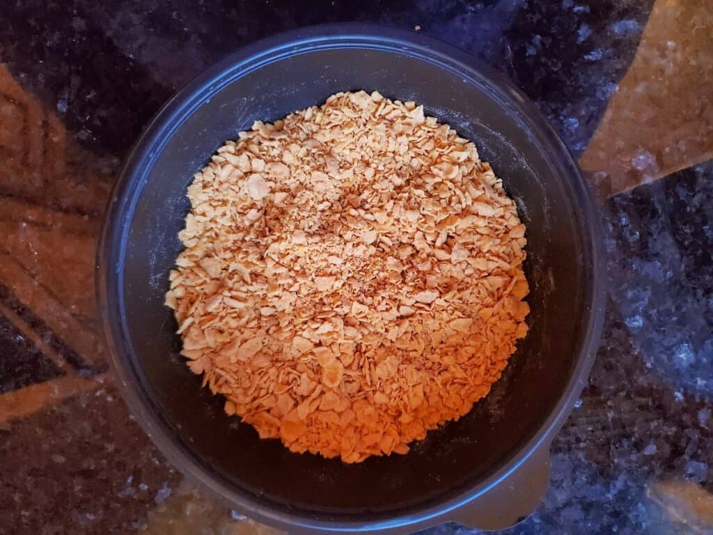 Corn flakes crushed in a black bowl.