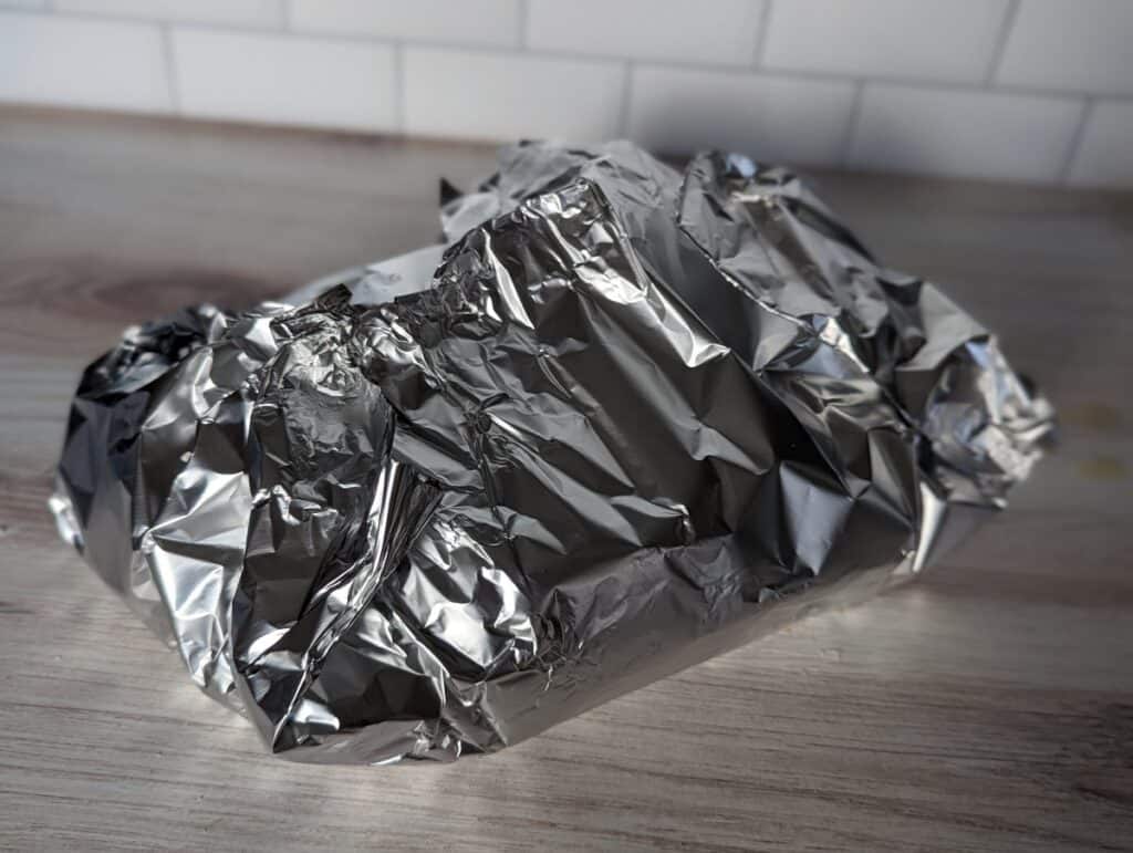 Loaf of bread loosely wrapped in foil on a counter.