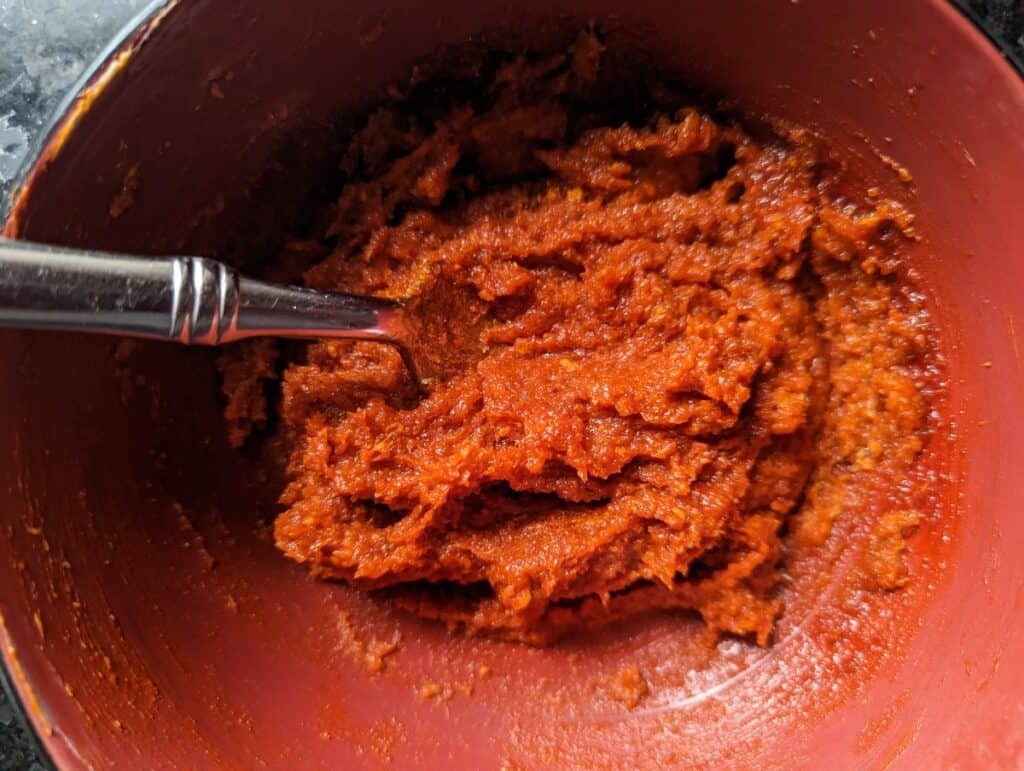 Orange bowl with gochujang caramel sauce and fork in the bowl.
