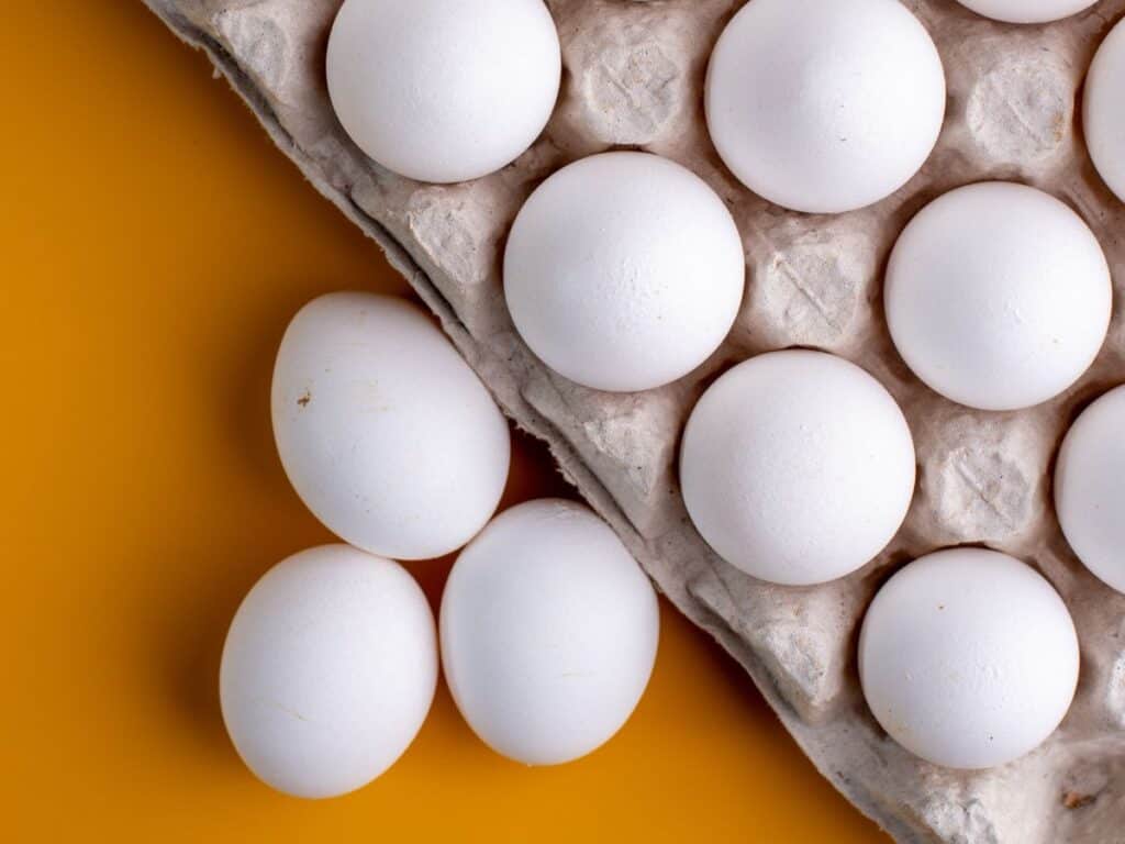 Overhead of white eggs in and next to a carton.