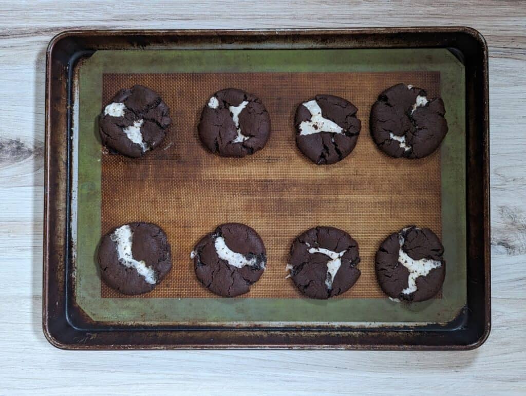 Overhead shot of chocolate marshmallow cookies on a cookie sheet sitting on a wooden board.