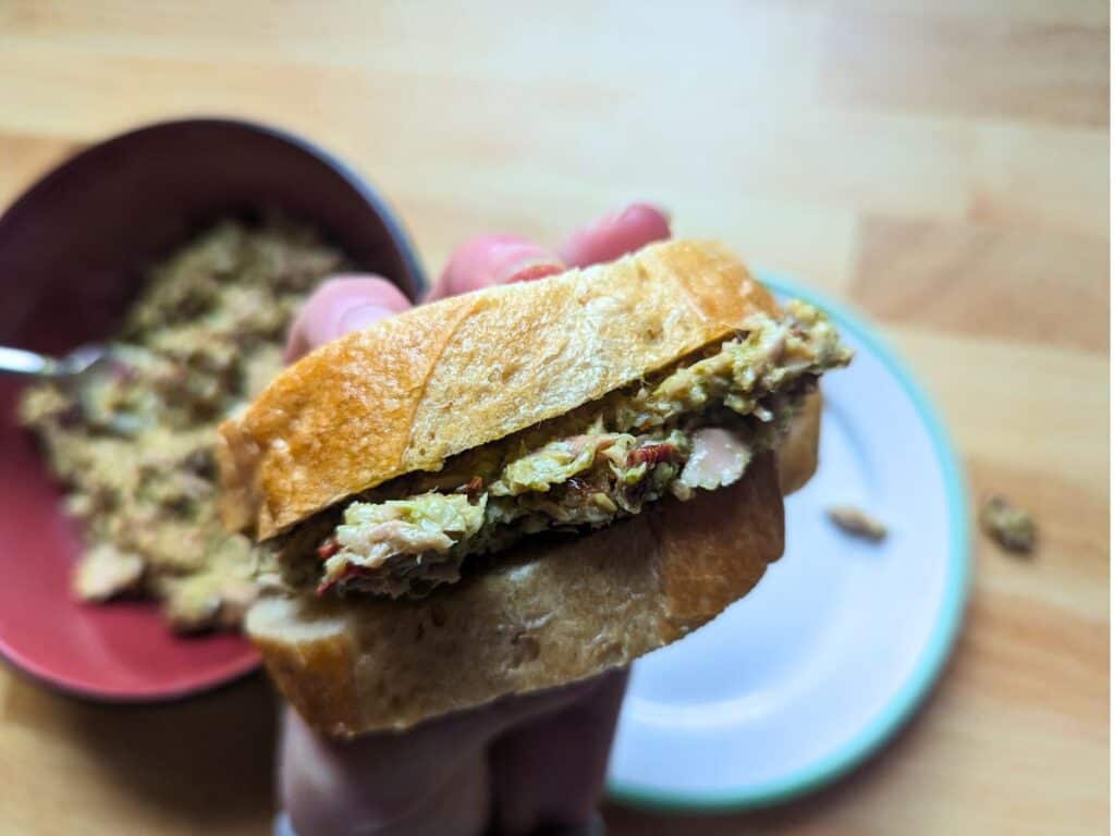 Image shows a hand Holding a tuna salad sandwich.