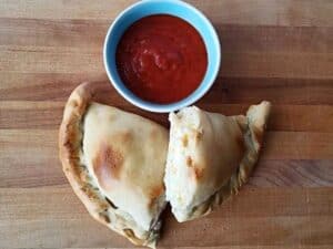 Image shows calzones with a small bowl of sauce.