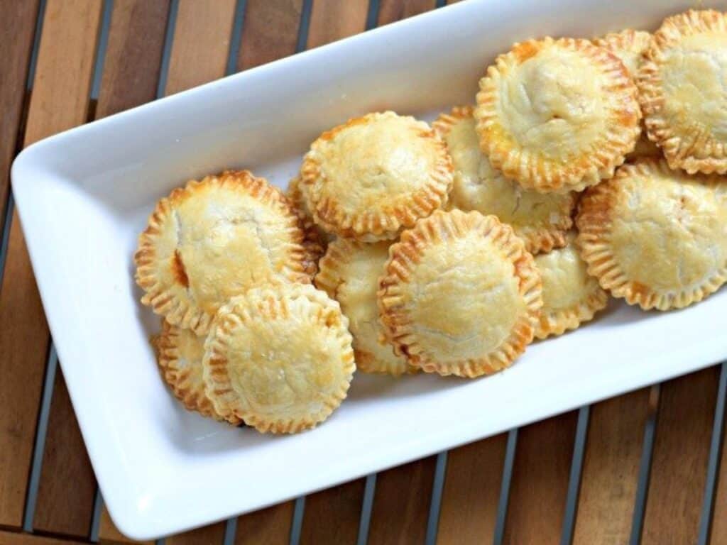 Image shows chicken empanadas served on a plate on a wooden table.