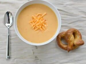Image shows delicious instant pot beer cheese soup with homemade pretzel.