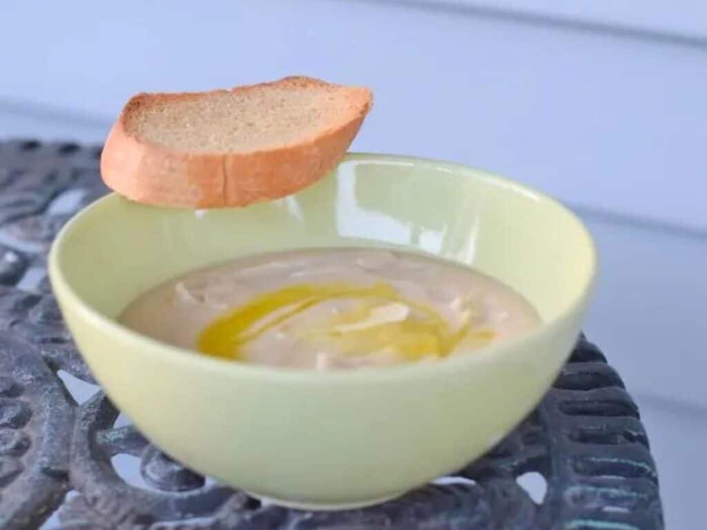 Image shows easy to make creamy Tuscan bean soup in a bowl with crostini.