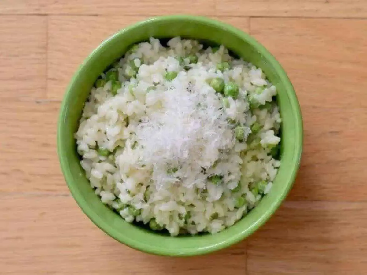 Image shows a Spoonful of risotto with peas and lemon with the rest of the bowl in the background.