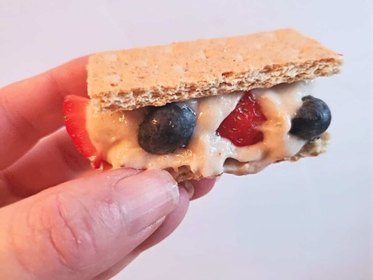 Image shows Banana ice cream sandwiches with strawberries and blueberries on a wooden board.
