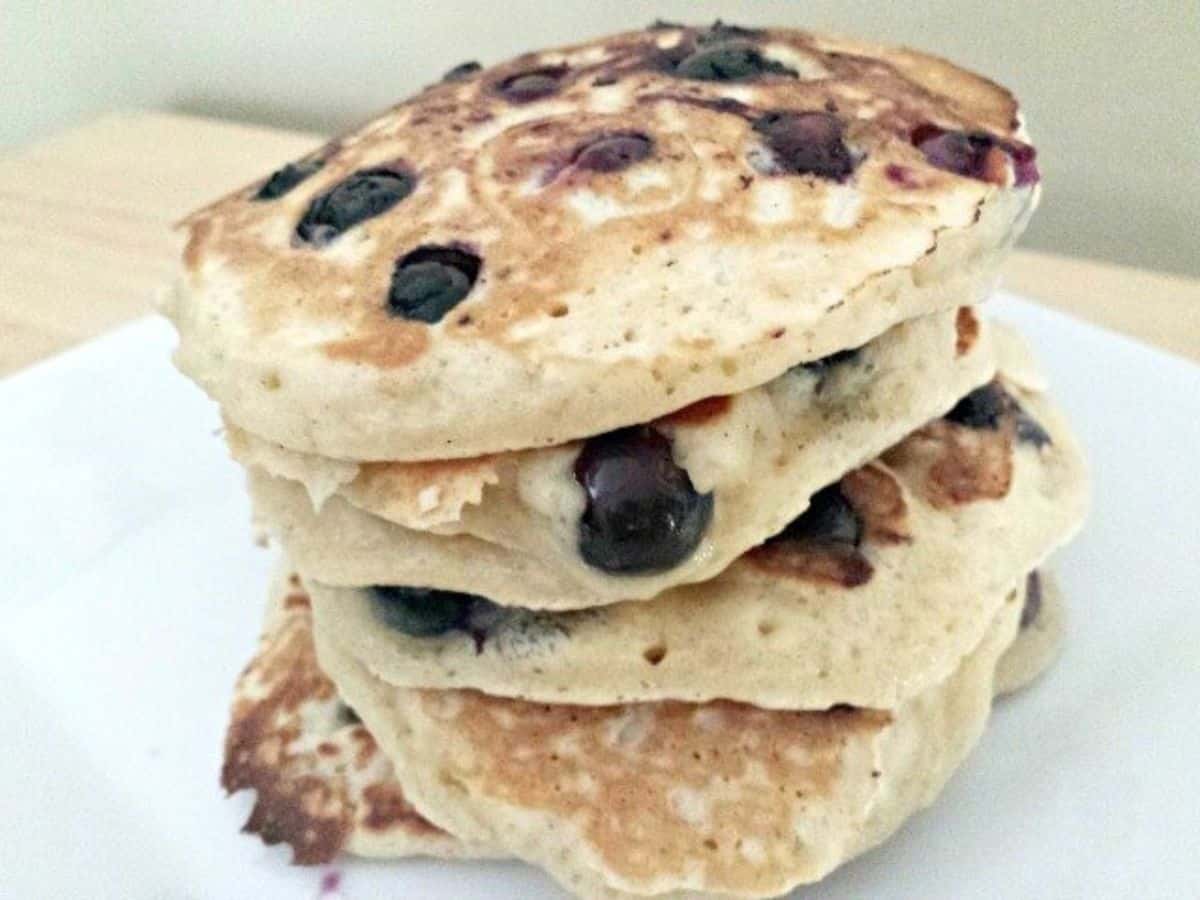 Image shows blueberry pancakes stacked on a white plate.