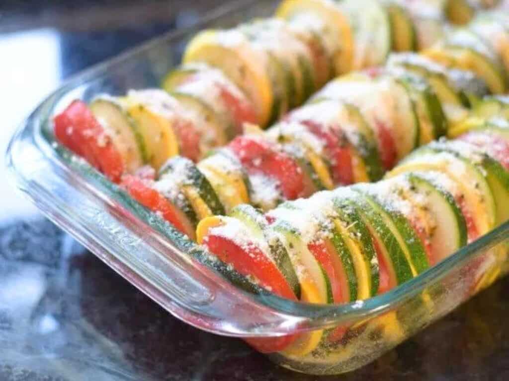 Image shows sprinkling parmesan to the sliced vegetables of ratatouille with an Italian flair.
