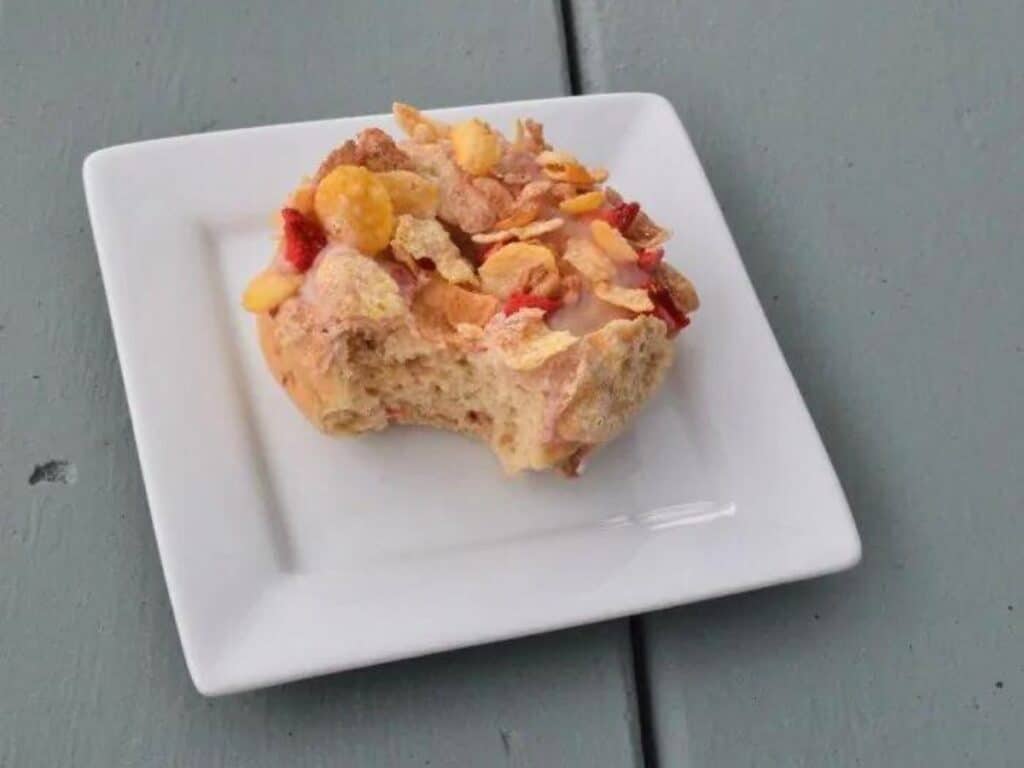 Image shows strawberry cereal donut served on a plate.