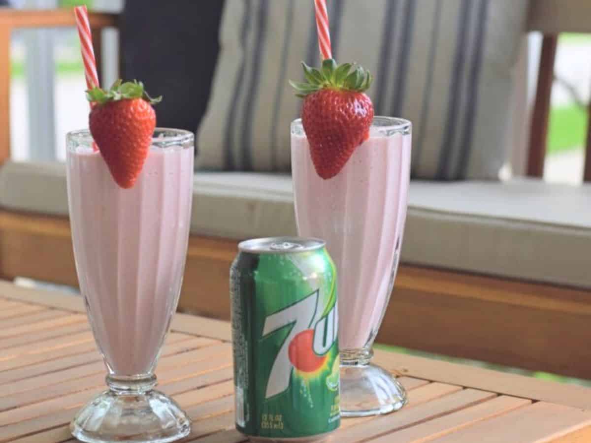 Two milkshake glasses with frozen strawberry lemonade garnished with strawberries sitting on a wooden table outside.