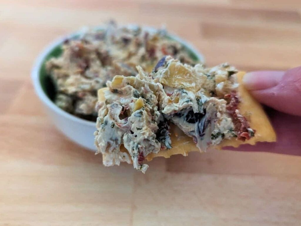 Image shows yummy bite of Tuscan artichoke and sundried tomato dip.