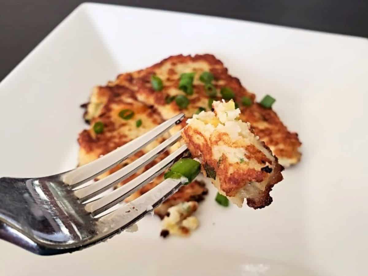 Image shows A plate of loaded mashed potato pancakes with green onions on it.