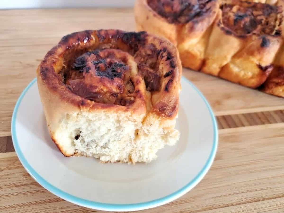 Image shows a three quarters angle shot of a Savory Pulled Pork Cinnamon Roll on a small plate with the rest of the batch behind it.