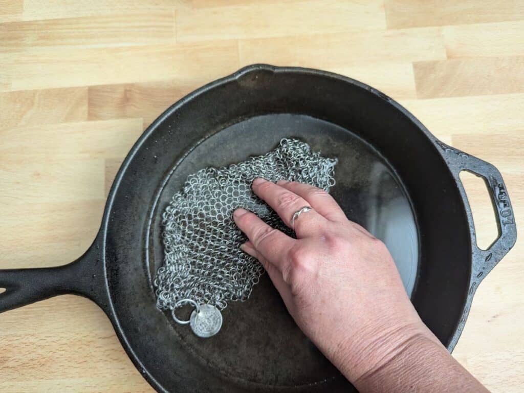 Image shows a Hand using a chain mail sponge to clean cast iron.