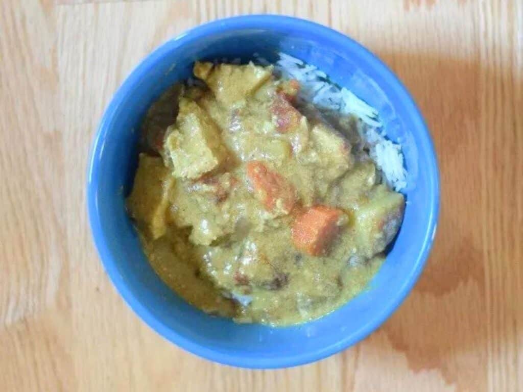 Image shows irresistible chicken curry in a bowl on top of rice.
