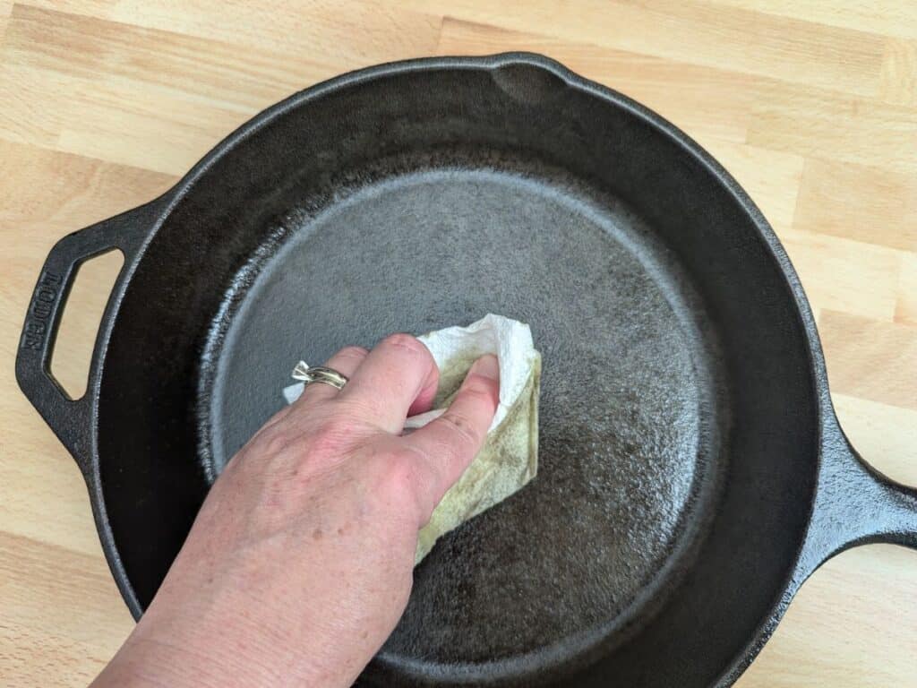 Image shows the Overhead of hand oiling a cast iron pan.