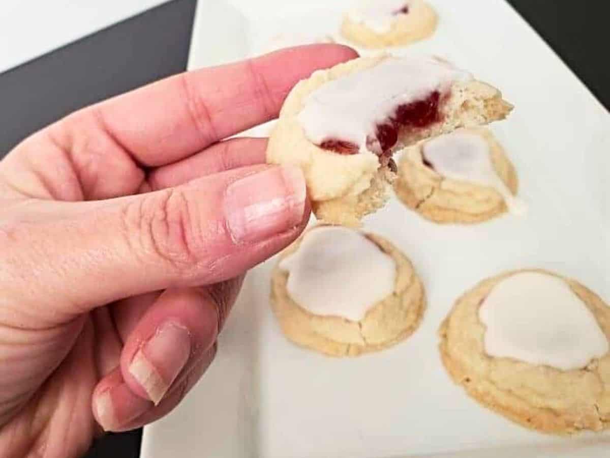 A thumbprint cookie with a bite taken out, showing the jam center under the glaze.