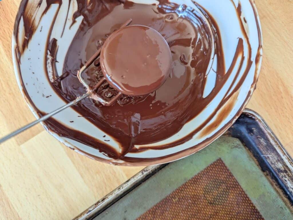 Image shows  a Cookie being dipped in chocolate.