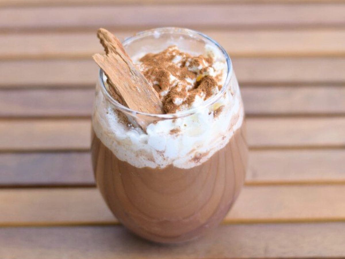 Image shows a Spicy Cinnamon Mocha in a clear glass with a cinnamon stick in the foam.